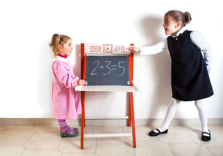 Little girl teaching mathematics to a younger child next to the chalkboardの写真素材