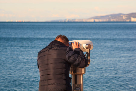 TRIESTE, ITALY - DICEMBER, 17: Man looking through a tourist binoculars next to the sea in Trieste...