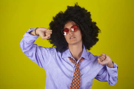 Beautiful indian girl with afro curly hairstyle and male clothes waking up and stretching on yellow backgroundの写真素材