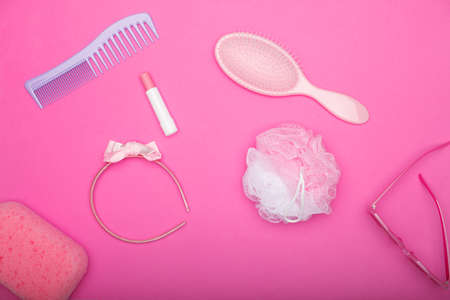 Flat lay composition of pink female bathroom accessories lying on a pink field. Accessories of every woman including lipstick, hairbrush, sunglasses, sponge, comb and headbandの写真素材