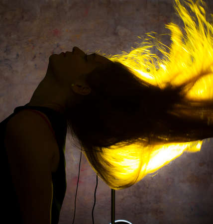Portrait against the gold light of a young beautiful woman posing on blue backgroundの写真素材