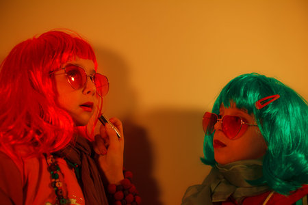 Two beautiful kids play cosmetics, paint lips with lipstick getting ready for the nightclub. Disco...