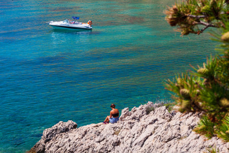 Stara Baska, Croatia - July, 22: Girl reading a book sitting on the rock next to the sea on July 22, 2020のeditorial素材
