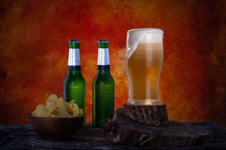 Glass of fresh pint beer with foam next to two green bottles of lager beer. Bottles and glass with water drops.の写真素材