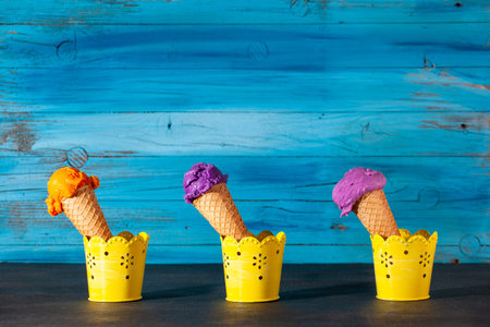 Three ice cream cones on old wooden blue background. The scoops are assorted of blueberry,...