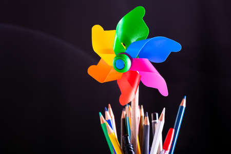 Pinwheel and pencils pot on stacked books, school supplies on white desk with blackboard texture in background. Side view, copy space, close-up. Learning, education conceptの写真素材