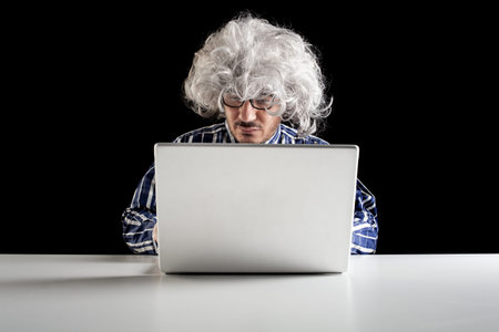 A boomer senior-focused concentrated sit at the desk looking at laptop computer on black background