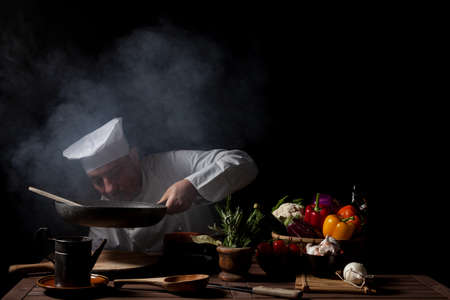 Male cook in white uniform and hat while working in a restaurant kitchen while the cooking fumes invade the kitchenの写真素材