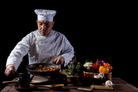 Male cook in white uniform and hat while working in a restaurant kitchen. On the table vegetables and herbs ingredientsの写真素材