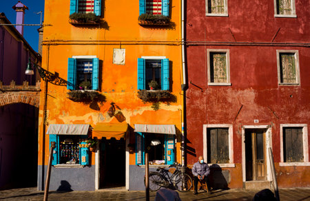 Burano, Italy- January, 06: Italian elderly man sitting outside his house next his bicycle, behind the colorful houses of Burano island on January 06, 2022のeditorial素材