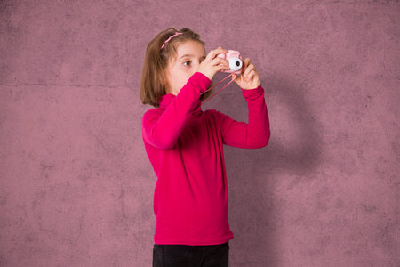 Little Girl Taking Picture Using Toy Photo Camera on pink background