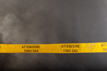 Yellow emergency sign of attention gas pipe on smoke-filled background. On the yellow tape the written notice "attention gas tube"の写真素材