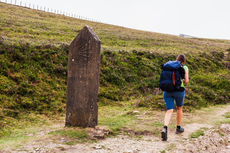 Pilgrim walking next to the Stone Post with Scallop Shell Symbol of the Pilgrimage in the Pilgrim Trail of the Way of St James or Camino de Santiago. French Pyreneesの写真素材