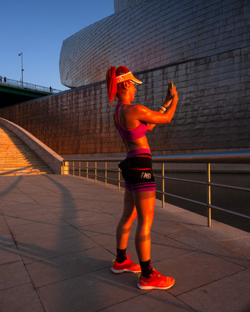 Bilbao, Spain - August 02, 2022: Fit tanned woman in sportswear with perfect body take photo selfie...