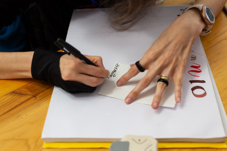 Close-up of the hands of an experienced calligrapher woman practicing writing in Italian and in an ancient style, the date October 26th, on a sketchbookの写真素材