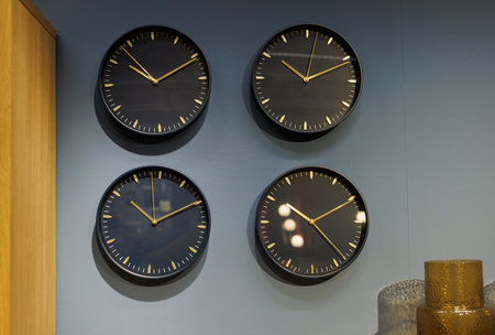 Multiple wall clocks displaying different times on a gray wall in a modern roomの写真素材