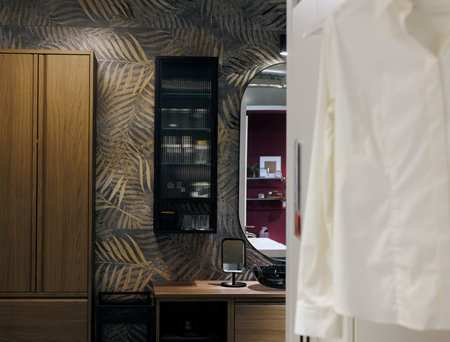 A stylish interior featuring a desk, cabinet, and mirror, complemented by a leaf-patterned wallpaper that adds a touch of nature to the room. The furniture creates a cozy and functional workspace with a modern, elegant atmosphereの写真素材