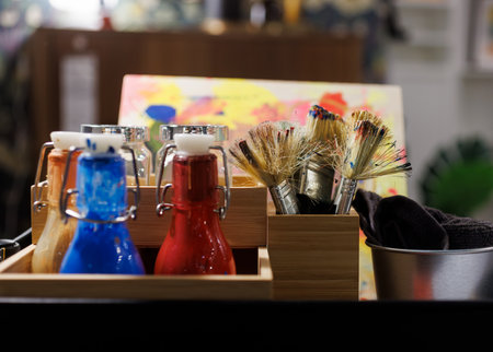 Close up of small bottles of colors blue and red and paintbrushes and art supplies on a messy table art studio. Art classes, creativity, art education, painting workshops, inspiration, artistic tools, creative environment.の写真素材