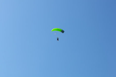 Bovec, Slovenia - July 17, 2025: A paraglider with a green parachute is descending down to Kanin, Slovenia, with a blue sky in the background.の写真素材