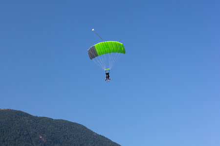 A paraglider with a green parachute is descending down to Kanin, Slovenia, with a blue sky in the background.の写真素材