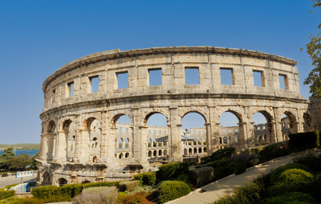 Ancient heritage in Pula, Istria, Croatia. Arches of monumental ancient Roman arena. Detail of historic amphitheater, wide angle view of high walls on blue sky background.の写真素材