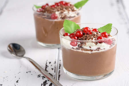 Chocolate mousse with currant and mint in a glasses on a whiite wooden backgroundの写真素材