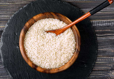Isolated handful of raw rice in the wood bowl on black stone backgroundの写真素材