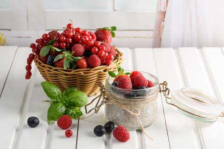 Healthy blended smoothie made from almond milk. Glass jar with chia pudding with fresh strawberries, raspberries and blueberries. Basket with berries. On a wooden light background.の写真素材