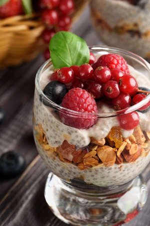 Two glasses of chia pudding with fresh strawberries, raspberries and blueberries. Basket with berries. On a wooden grey background.の写真素材