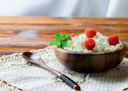 Cottage cheese with fresh raspberry in a wooden bowl on old wooden background with copy space for your text. Top viewの写真素材