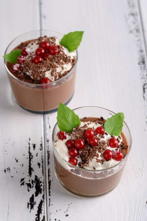 Chocolate mousse with currant and mint in a glasses on a whiite wooden backgroundの写真素材