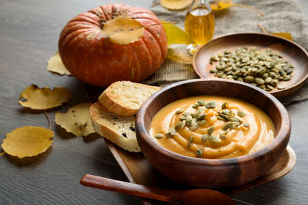 Pumpkin soup in a wooden bowl, with autumn leaves and pumpkinの写真素材