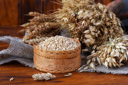 Grains of whole oats in a wicker box and ears of various cereals wheat, oats, rye and others on a wooden backgroundの写真素材