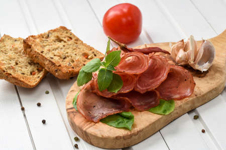 Salami smoked sausage slices basil leaves,peppercorns and bread toast on wooden board on white backgroundの写真素材