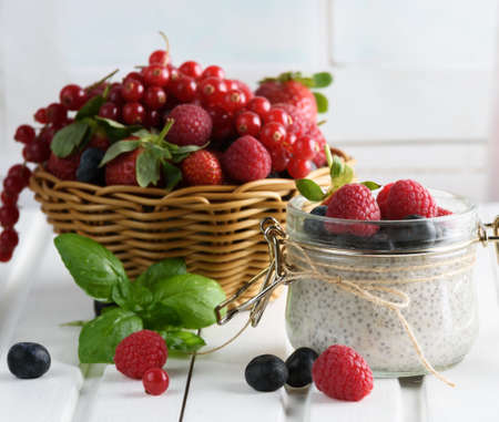 Healthy blended smoothie made from almond milk. Glass jar with chia pudding with fresh strawberries, raspberries and blueberries. Basket with berries. On a wooden light background.の写真素材