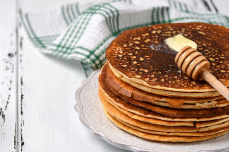 Stack of tasty pancakes with butter and honey for breakfast on vintage white plateの写真素材
