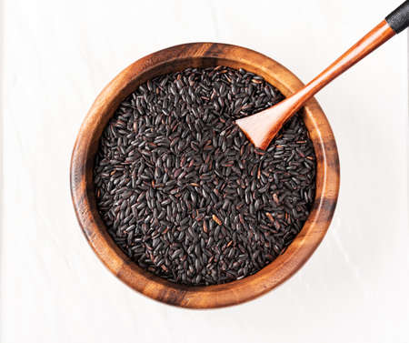 Isolated handful of raw black nero rice in the wood bowl on white backgroundの写真素材
