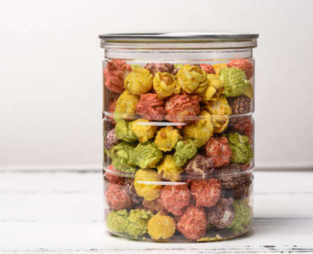 Colorful caramel popcorn in a glass jar on a white wooden background.の写真素材