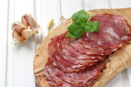 Salami smoked sausage slices basil leaves and peppercorns on wooden board on white backgroundの写真素材