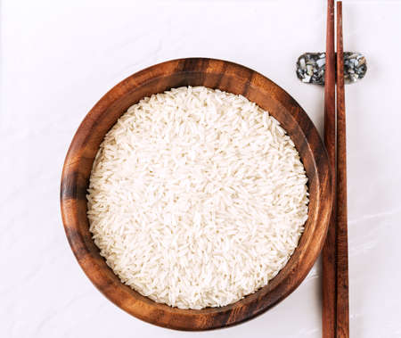 Isolated handful of raw rice in the wood bowl on white background.の写真素材