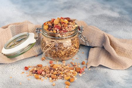 Healthy breakfast - glass jars of oat flakes,granola with dried fruit, berries and nuts on light...