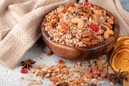Wooden Bowl with granola with nuts, dried crandberries and dried orenge on a old light table.の写真素材