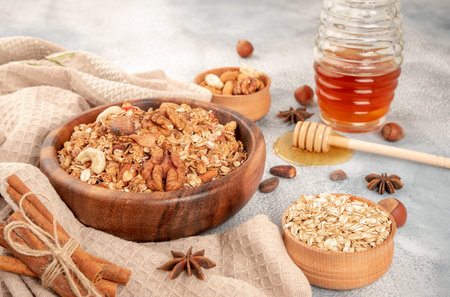 Homemade granola in wooden bowl with ingredients - oat, nuts, honey and spice cinnamon and anise.