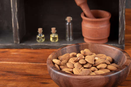 Almonds in wooden bowl on dark background with glass bottles - almond's oilの写真素材