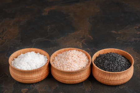 White (sea), pink (himalayan) and black salts in wooden bowls on dark background.の写真素材