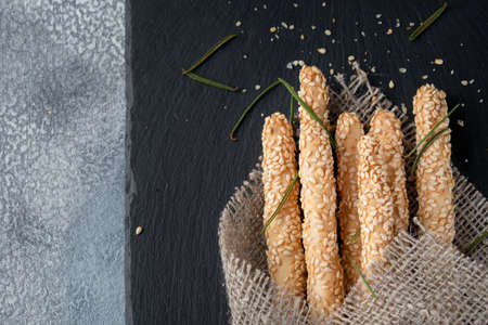 Top view of traditional italian appetizer grissini with sesame on black slate board and marble background with copy space.の写真素材