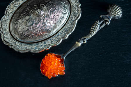 Red caviar in silver bowl and silver spoon on black background.の写真素材