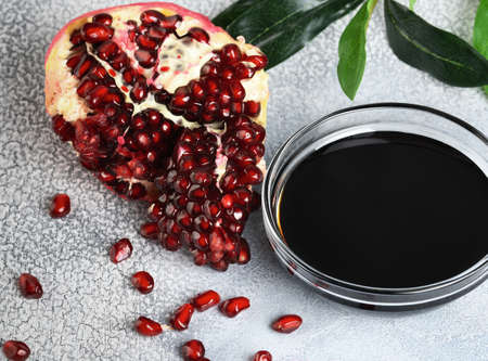 Saucer with pomegranate sauce with fresh ripe pomegranate fruits with leaves on a light rustic background.の写真素材
