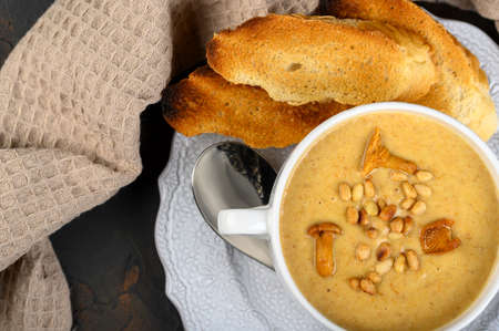 Mushroom, chanterelle cream soup with pine nuts and croutons on dark background. Top view, copy spaceの写真素材