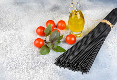 Raw black pasta with basil, tomatoes and olive oil on light background. High quality photoの写真素材